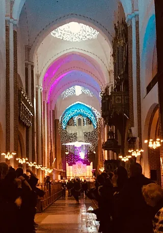 Kircheninnenraum mit bunten Lichtern und Besuchern.