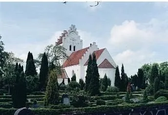 Weiße Kirche mit rotem Dach und Friedhof.