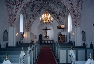 Kircheninnenraum mit bemalter Decke, Bänken und Altar.